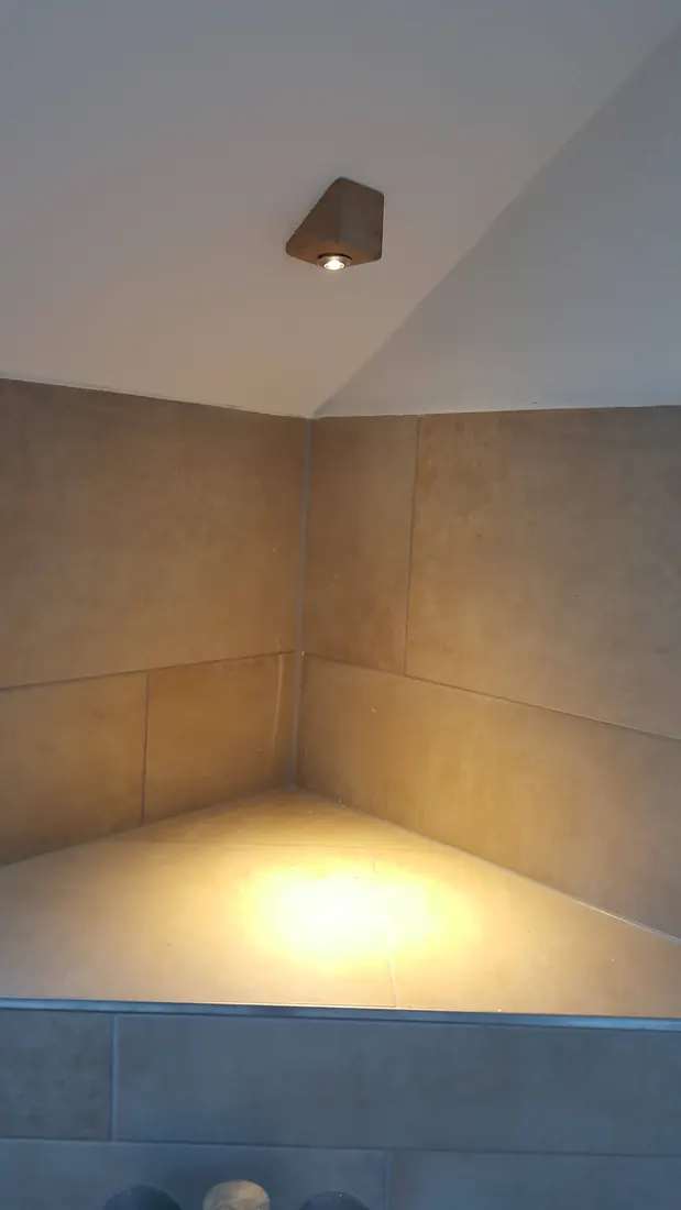 Gefliester Duschbereich unter einer Dachschräge mit warmem Deckenlicht